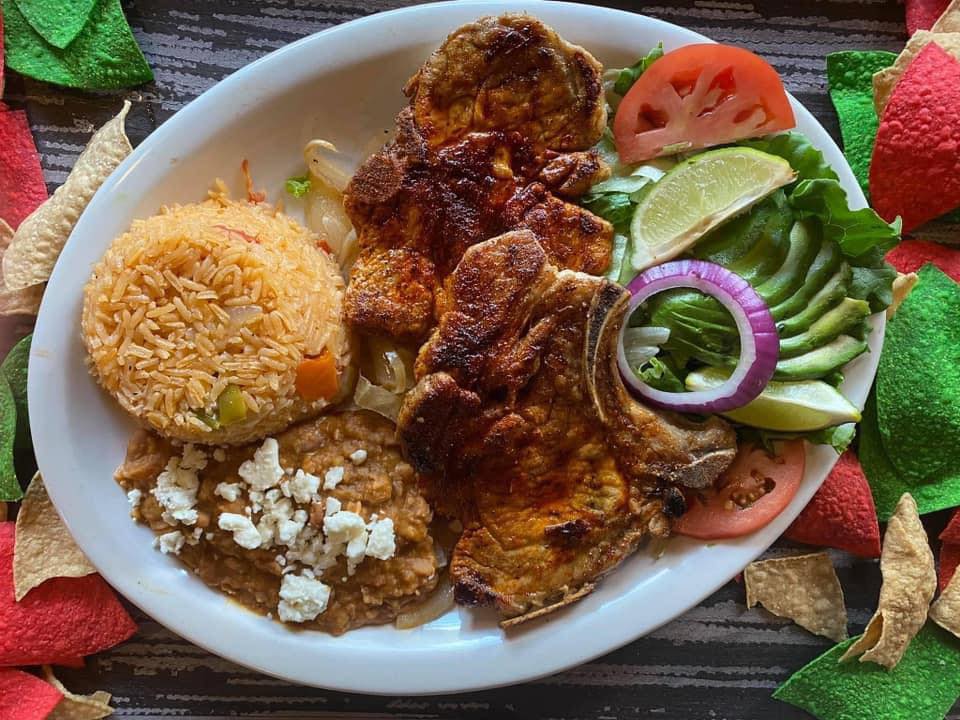 Grilled bone-in pork chops with Mexican rice, refried beans, avocado, and fresh salad